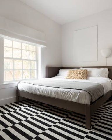 Bright bedroom with dark wood bed, white bedding, black and white striped rug, and large window with white trim