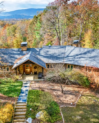 Modern stone and wood house with slate roof nestled in autumn forest with distant mountain view