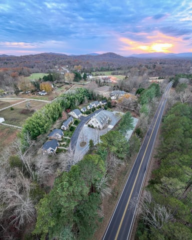 Aerial view of rural valley with homes, road, river, and forested hills at sunset