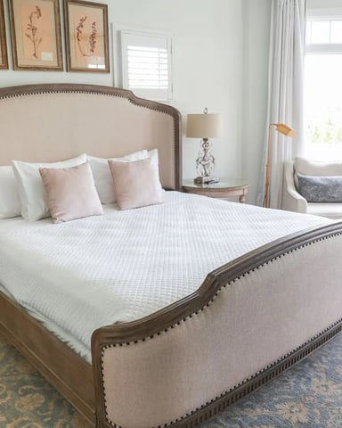 Bright master bedroom with upholstered bed, large windows, seating area, and hardwood floors