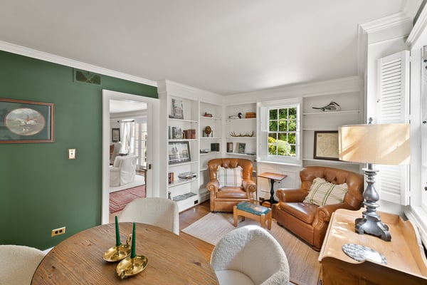 Living room with built-in white shelving, brown leather chairs, coral sofa, framed artwork, and striped red rug