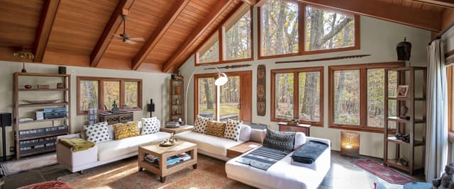 Modern cabin with blue-gray roof nestled in autumn forest with mountain view in background